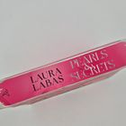 Der Text "LAURA LABAS PEARLS & SECRETS" ist auf einem pinken Buchrücken zu sehen. Ein kleines Symbol ist ebenfalls abgebildet.