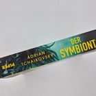 Buchrücken mit Text: "DER SYMBIONT, ADRIAN TCHAIKOVSKY, PIPER." Hintergrund zeigt tentakelartige Muster in Dunkel- und Grüntönen.