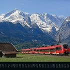 "Mai" und Kalendertage unten; roter Zug vor schneebedeckten Bergen und Wiesenhütte; blauer Himmel.
