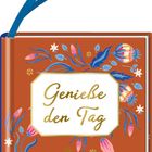 „Genieße den Tag“ steht auf einem orangefarbenen Notizbuch mit blauen Blumen und einer blauen Schlaufe.