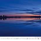 März-Kalender mit Landschaft: Ein ruhiger See spiegelt den farbenfrohen Sonnenuntergang wider, Bäume am Horizont.