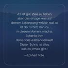 „Es ist gut, Ziele zu haben… was es jemals gibt." – Eckhart Tolle. Hintergrund: dunkler See mit Bergen.