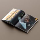 Text: "HELIO COPTA". Geöffnetes Magazin mit einem Foto eines Mannes mit Hut und Kopfhörern. QR-Code in der Ecke.