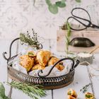 Gebackene Teigtaschen mit grüner Füllung auf rustikalem Tablett, dekoriert mit Kräutern; im Hintergrund Küchendeko.