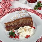 Ein Stück Kuchen mit Puderzucker, Sahne und Preiselbeeren auf einem weißen Teller, umgeben von rot-weißem Stoff.