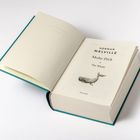 HERMAN MELVILLE Moby-Dick or The Whale. Ein Buch mit offenem grünen Einband und einem Wal auf der Seite.