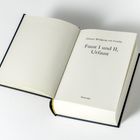 Der Text auf der Buchseite lautet: "Johann Wolfgang von Goethe, Faust I und II, Urfaust, Anaconda." Ein offenes Buch auf weißem Hintergrund.