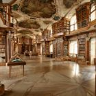 Ein prächtiger Bibliothekssaal mit kunstvollen Deckenmalereien, hohen Bücherregalen und großen Fenstern.