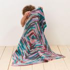 Ein Kind verdeckt sein Gesicht mit einer bunten, gehäkelten Decke in kräftigen, abwechslungsreichen Farben. 