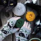Handstulpen mit schwarzen Katzenmotiven, grüne Wolle. Schwarze Katzen, gelbe und graue Wollknäuel, Tasse Tee.