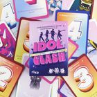 "IDOL CLASH: Sei der Star am K-Pop-Himmel" steht auf einer Kartenschachtel, umgeben von bunten Karten mit Zahlen und Illustrationen.