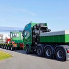 Text: "Kübler Spedition". Ein langer Schwertransporter mit grüner Kabine und Anhänger auf einer Straße unter blauem Himmel.