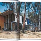 Aufgeschlagenes Buch mit Architekturillustration: Modernes, würfelförmiges Gebäude im Wald mit Glas- und Holzelementen.