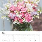 Kalenderseite für März mit hervorgehobenen Tagen: Internationaler Frauentag am 8., Frühlingsanfang am 20., Ostern am 28. Ein Glasvase voller rosa Rosen und Maiglöckchen.