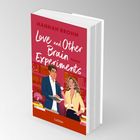 Auf einem roten Buchcover steht: "Hannah Brohm, Love and Other Brain Experiments, Roman, Lübbe". Illustration: Mann und Frau in Bibliothek.
