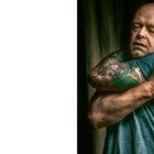 Auf Seite 14 hält ein Mann mit geschlossenen Augen seine Schultern. Er trägt ein gestreiftes Shirt; Tattoo am Arm sichtbar.