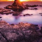 3, 2027, März-Kalender. Sonnenuntergang hinter Felsen am Meer, leuchtender Himmel in Orange- und Lilatönen.