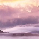 Monat März 2017, Landschaft: Hütten auf nebelbedeckten Wiesen vor Bergkulisse bei Sonnenaufgang.