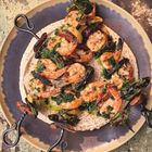 Ein Teller mit Garnelenspießen auf Hummus mit Kräutern. Die Oberfläche wirkt rustikal und abgenutzt.