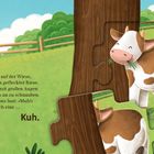 Ein weiß-hellbrauner Riese kaut friedlich und ruft "Muh". Illustration zeigt eine Kuh auf einer grünen Wiese.