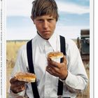 Text: "AROUND THE WORLD IN 125 YEARS".  
Ein junger Mann in Hemd und Hosenträgern hält zwei Brotscheiben.