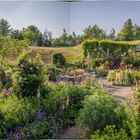 Der Garten zeigt eine Terrasse mit Tisch, Stühlen, bunten Blumen und Büschen, umgeben von Bäumen und Natur.