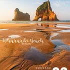 "Wharariki Beach, New Zealand." Eine Küstenlandschaft mit Felsen im Wasser, Sand und einem blau-grauen Himmel.