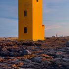 Leuchtturm Stafnes auf der Reykjanes-Halbinsel - Island. Ein gelber Leuchtturm steht auf felsigem Boden nahe Wasser.
