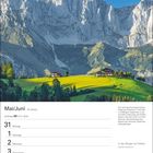 Mai/Juni, 22. Woche. Zitat: "In den Bergen ist Freiheit." Hochgebirge mit grünen Hügeln und zwei Häusern im Vordergrund.