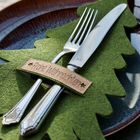 "Gedruckt: Frohe Weihnachten" auf einem grünen Filz-Tannenbaum, mit Messer und Gabel auf einem Teller platziert.