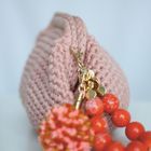 Keine sichtbaren Texte. Ein rosa gestricktes Täschchen mit einem goldenen Verschluss und rotem Kugelanhänger.
