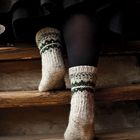 Eine Person geht in wollenen Socken eine Holztreppe hinauf, trägt dunkle Strumpfhose und einen Rock.