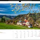 Märzkalender zeigt Kloster St. Trudpert. Blühende Zweige, grüne Hügel, Kirche mit grünem Dach im Tal.
