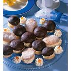 Keine Texte zu erwähnen. Auf einem blauen Teller sind mehrere mit Schokolade überzogene Gebäckstücke, dekoriert mit Sahnetupfern. Daneben eine Tasse Kaffee.