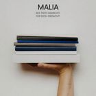 „MALIA. Aus Tiefe gemacht. Für dich gedacht.“ Eine Hand hält gestapelte Bücher, am Arm ein Punktmuster.