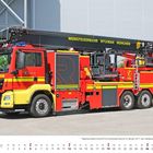 Auf der roten Feuerwehrfahrzeugseite steht "WERKFEUERWEHR MTU/MAN MÜNCHEN". Teleskopmastbühne in einer Industrieumgebung.