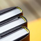 Drei Buchrücken, Nahaufnahme, weißes Papier und gelbe Lesebändchen sichtbar, Hintergrund unscharf.