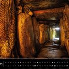 "Bretagne 03" unten. Ein langer, schmaler Steinkorridor mit höhlenartigen Gravuren und hellem Licht am Ende.