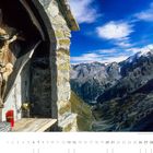 "Wegkreuz oberhalb des Stilfserjochs mit Blick auf den Ortler." Ein Kreuz mit Kruzifix neben Alpenlandschaft. Unten Kalender.