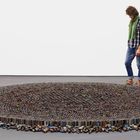 Ein Mann steht neben einer großen, runden Skulptur aus aufgestapelten Metallröhren.