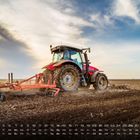 Kalender mit Tagen und Daten unten. Ein roter Traktor pflügt ein Feld unter einem blauen Himmel mit Wolken.