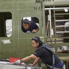 Zwei Arbeiter inspizieren das Innere eines grünen Flugzeugrumpfs. Einer schaut neugierig aus einem Fenster, beide sind konzentriert.