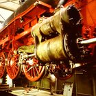 Aufschrift "532.25" und "53/1.20" auf einer großen dampfbetriebenen Lokomotivachse mit roten Rädern in einer Werkstatt.