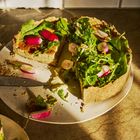 Ein Teller mit einer angeschnittenen Quiche, dekoriert mit frischen Radieschen und grünem Blattgemüse.