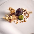 Keine Texte vorhanden. Eine kunstvolle Anordnung von Pilzen, Fleischstücken und einem grünen Gemüse auf weißem Teller.