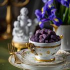 Ein Stapel edler Porzellanteller mit einer Tasse voller lila Trauben und daneben leuchtenden Irisblüten.