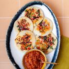 Kein Text. Fünf runde Pfannkuchen mit Gemüse und roter Dip-Sauce in Schale auf beigem Untergrund.