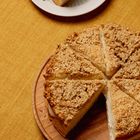 Ein Teller mit einem Stück Kuchen, dekoriert mit Sesamsamen. Daneben eine Kuchengabel auf einem gelben Tuch.