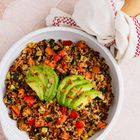 Schüssel mit Quinoa, buntem Gemüse und zwei Avocadoscheiben. Daneben ein Küchentuch mit rotem Muster.