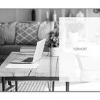 Text „VORWORT“. Ein Tisch mit Laptop, Papier und Pflanzen. Im Hintergrund ein Sofa mit Kissen.